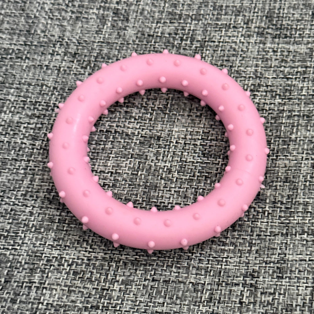Pink rubber dog chew ring with textured bumps on grey fabric background