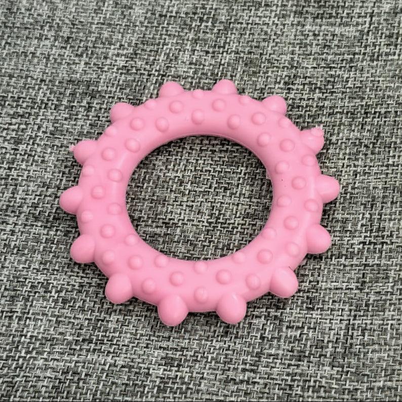 Pink spiked rubber dog chew toy ring on textured gray fabric background