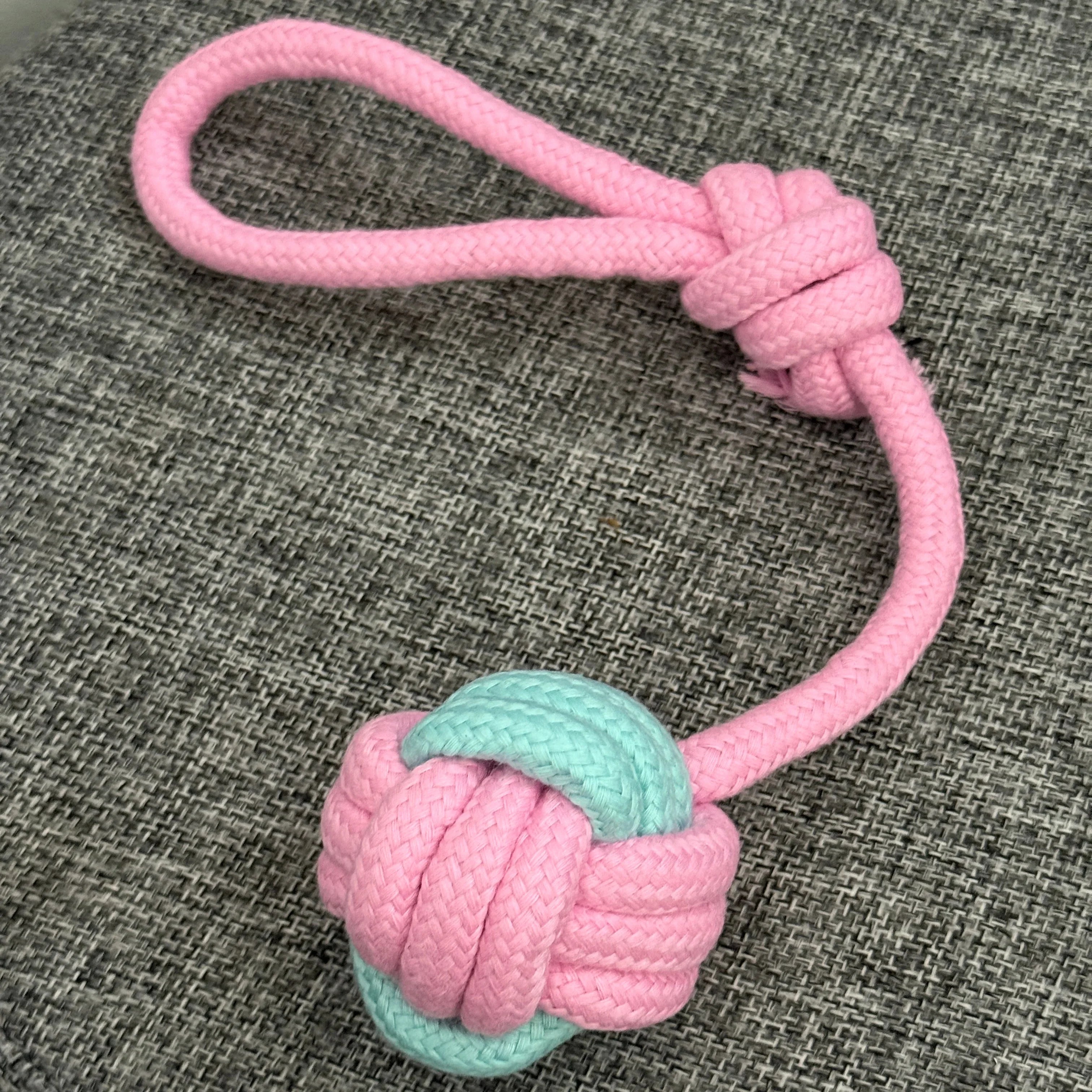 Pink and mint green rope dog toy with knot and loop on gray fabric background