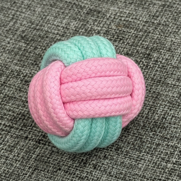 Pastel pink and blue rope ball dog toy on a grey fabric surface