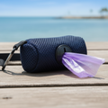 Navy blue dog waste bag dispenser with purple bags on wooden deck by the sea