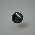 Round black pet accessory pin with metal clasp on grey background