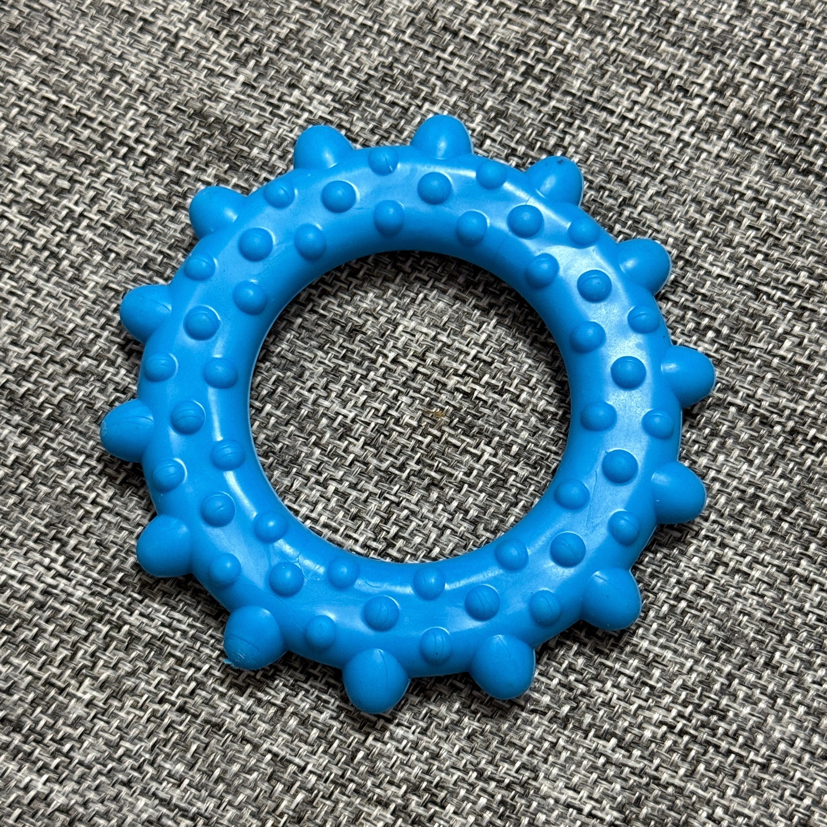 Blue rubber dog chew toy ring with textured spikes on a grey woven fabric background
