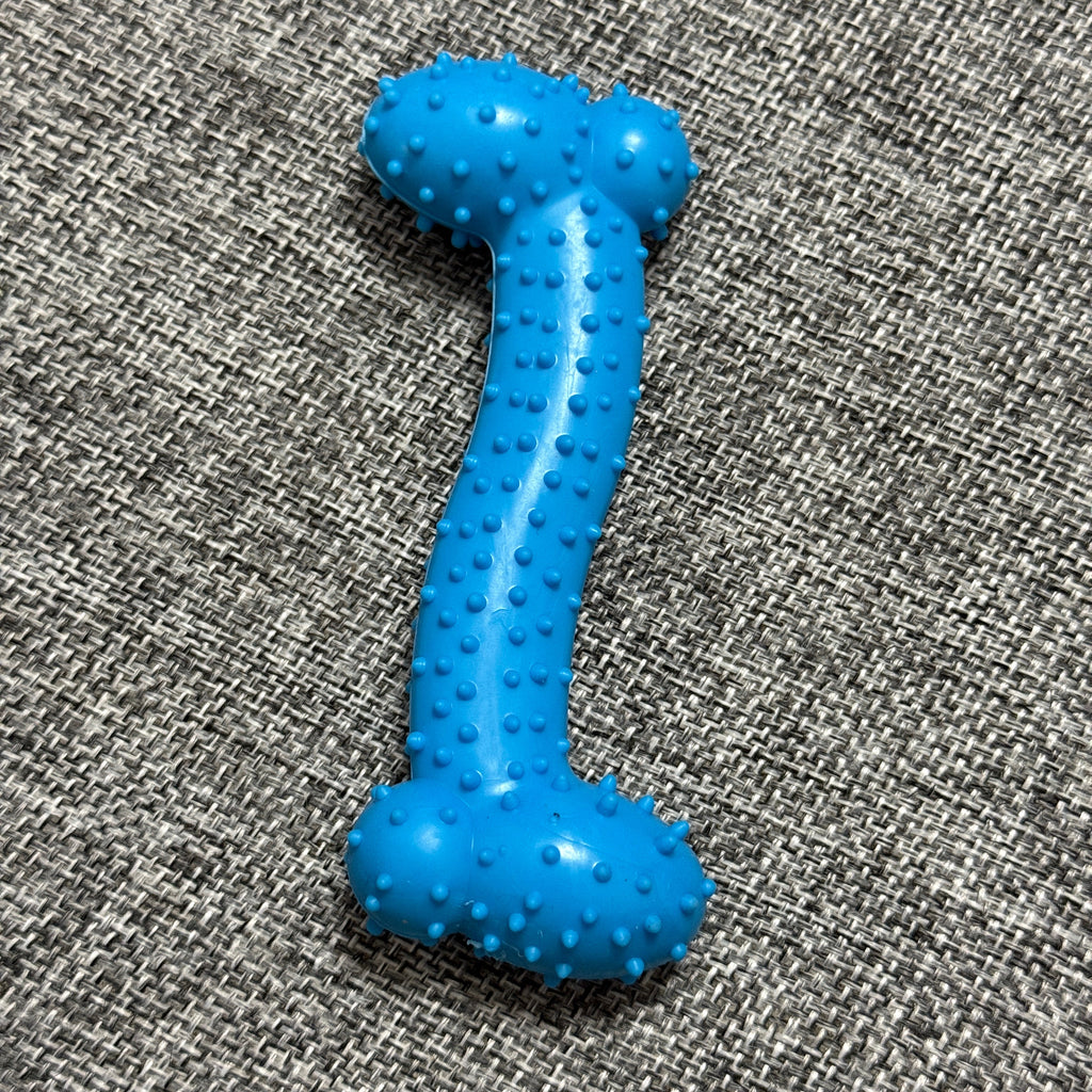 Blue rubber dog chew toy with textured bumps on a gray woven fabric surface