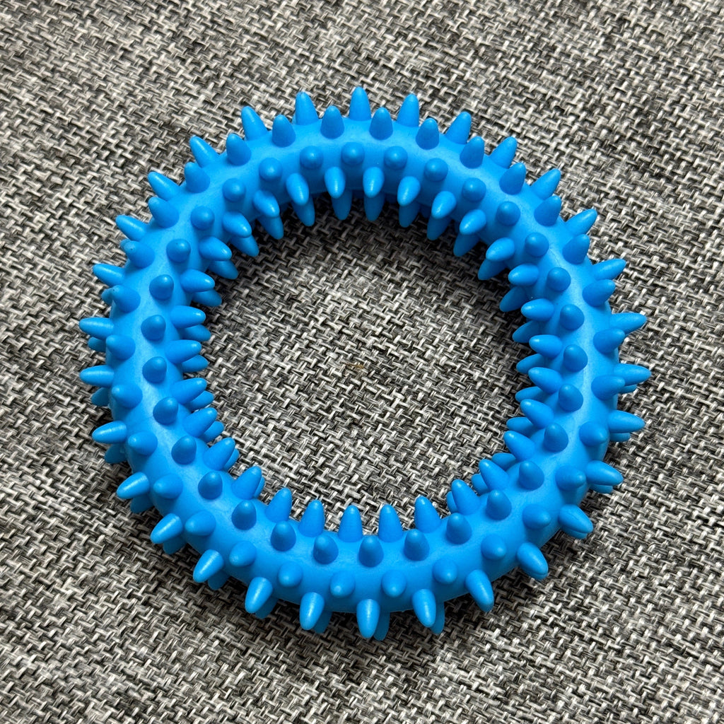 Blue spiky rubber dog chew ring on a textured grey fabric background