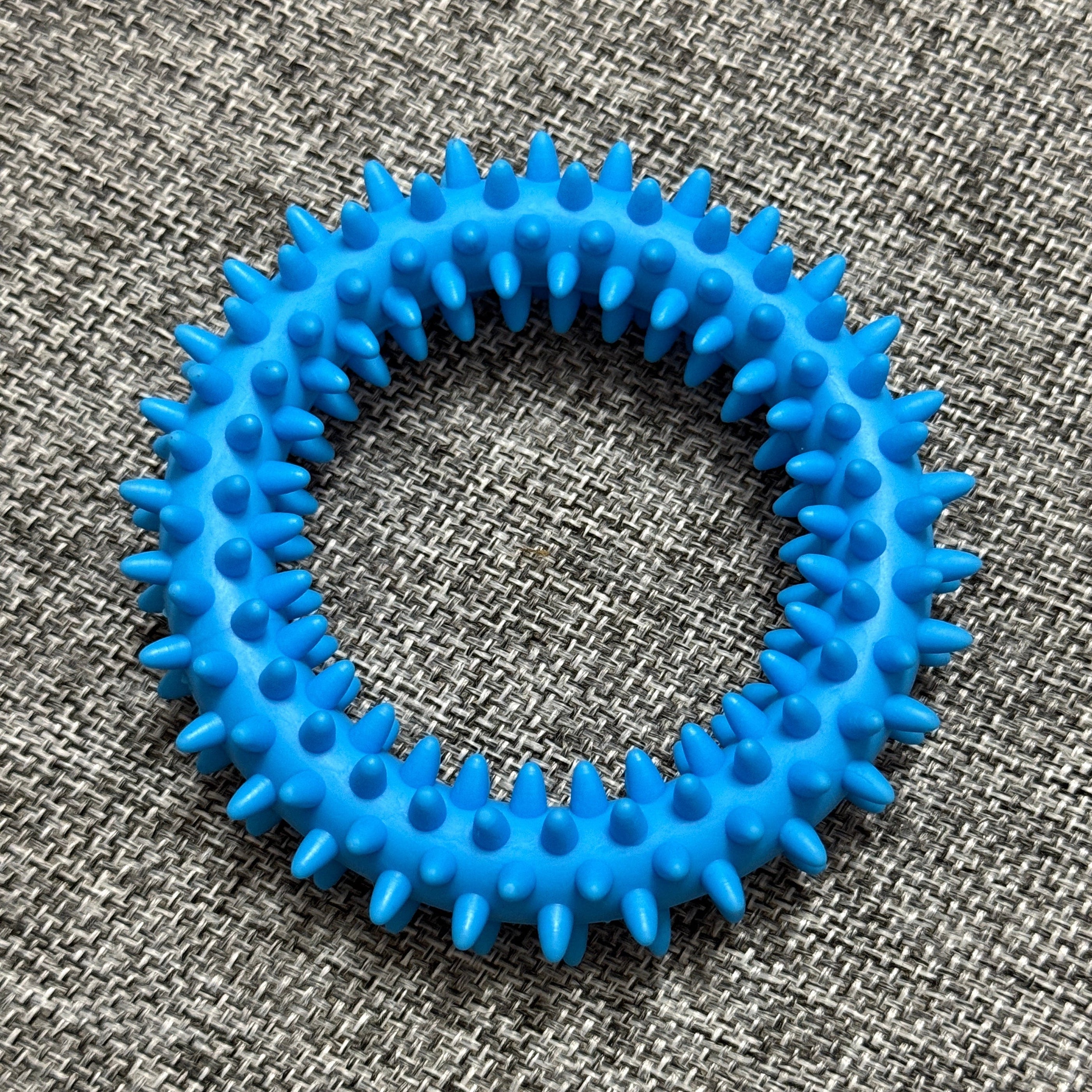 Blue spiky rubber dog chew ring on a textured grey fabric background