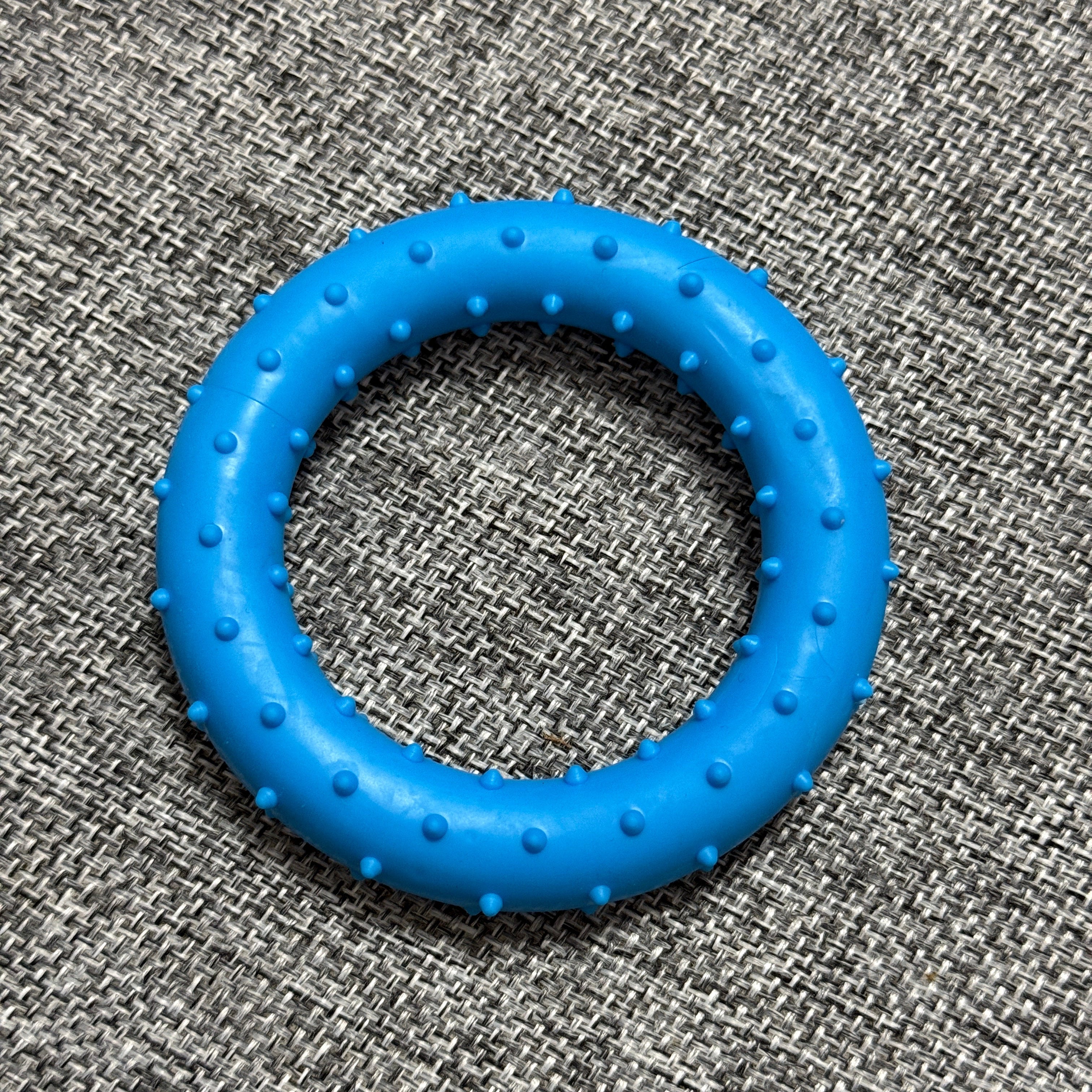 Blue rubber dog chew toy ring with textured bumps on grey woven fabric background