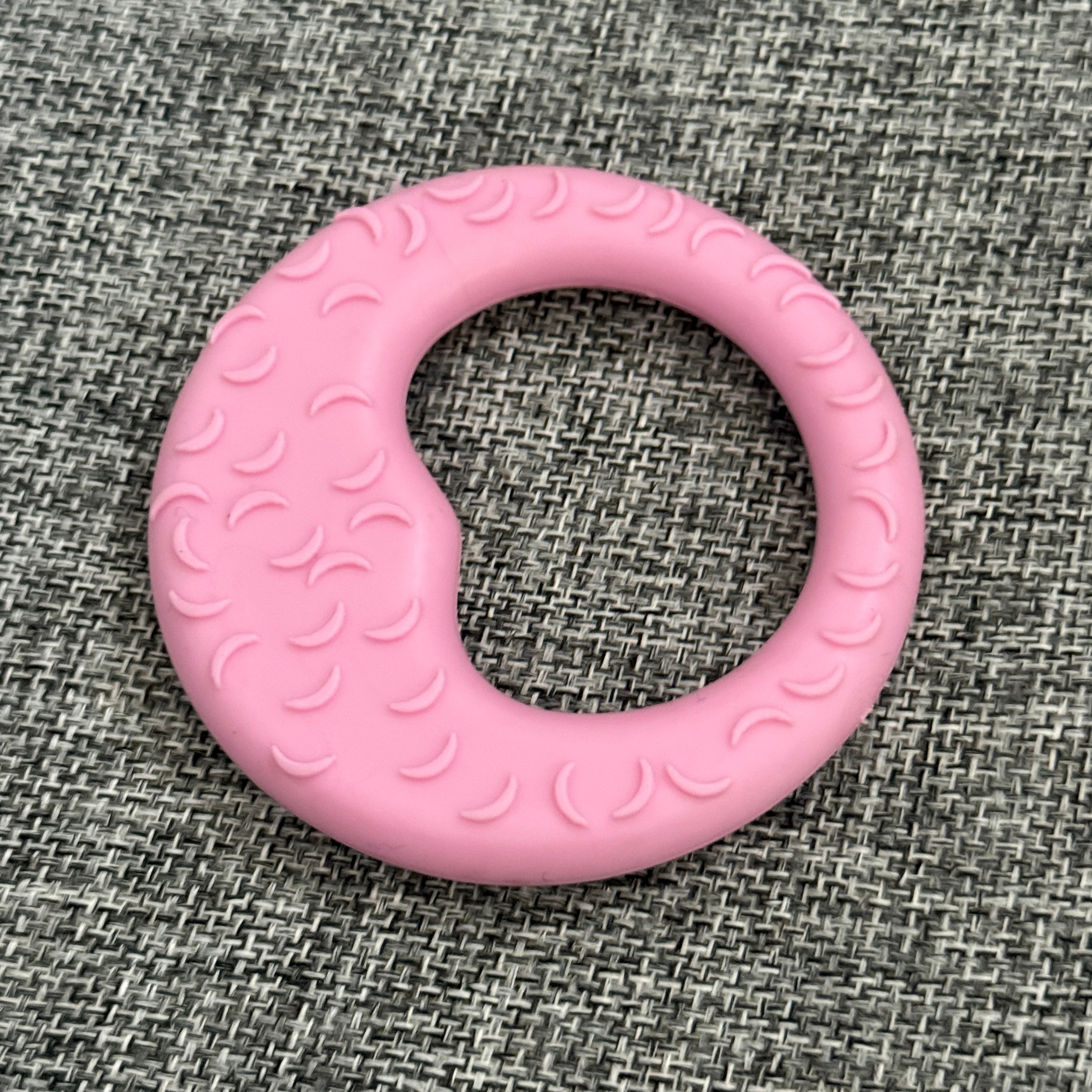 Pink textured pet chew toy ring on a gray fabric background