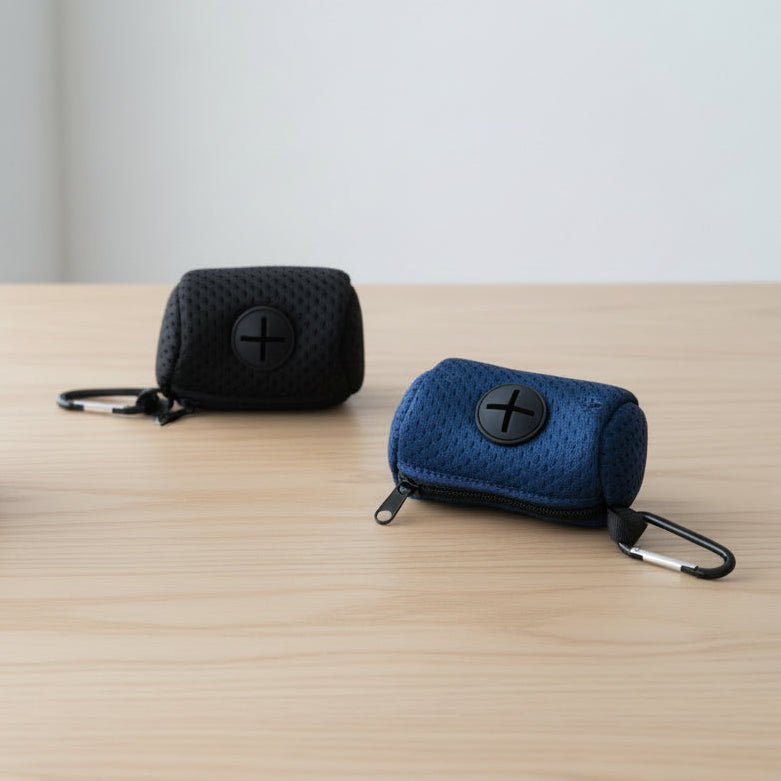 Black and navy blue pet waste bag holders with zippers and carabiner clips on a wooden table