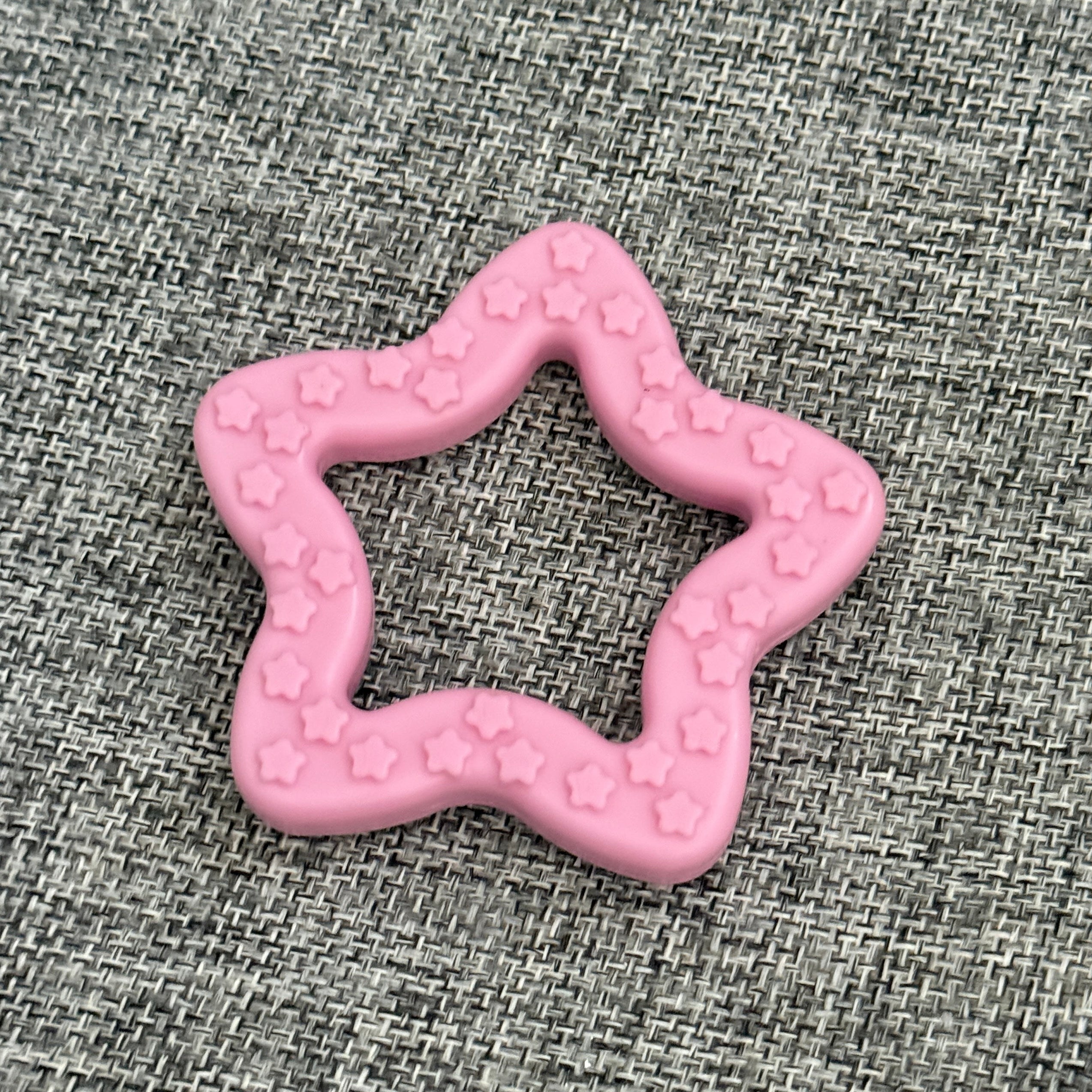 Pink star-shaped pet toy with small star patterns on a gray textured fabric background
