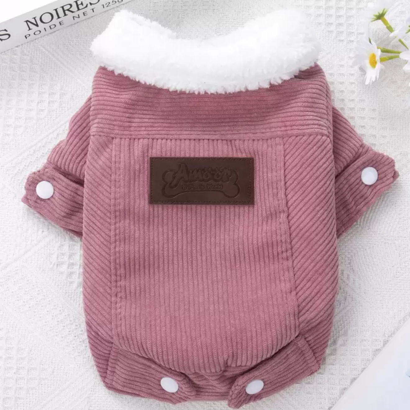 Pink corduroy dog jacket with white fleece collar and snap buttons, displayed on fabric.