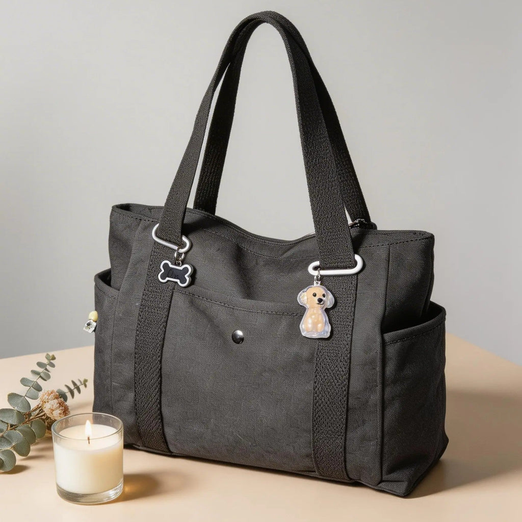 Black pet carrier tote bag with dog and bone charms, beside a lit candle on a beige table.