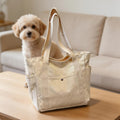 Small fluffy dog beside beige pet carrier bag on wooden table in cozy living room