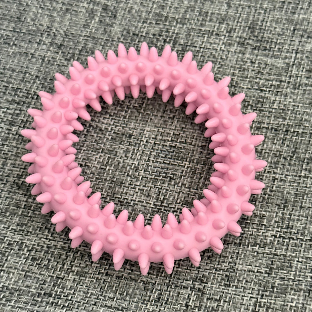 Pink spiked rubber dog chew toy ring on gray fabric background