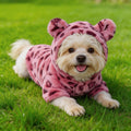 Small dog in pink leopard print hoodie with bear ears lying on green grass