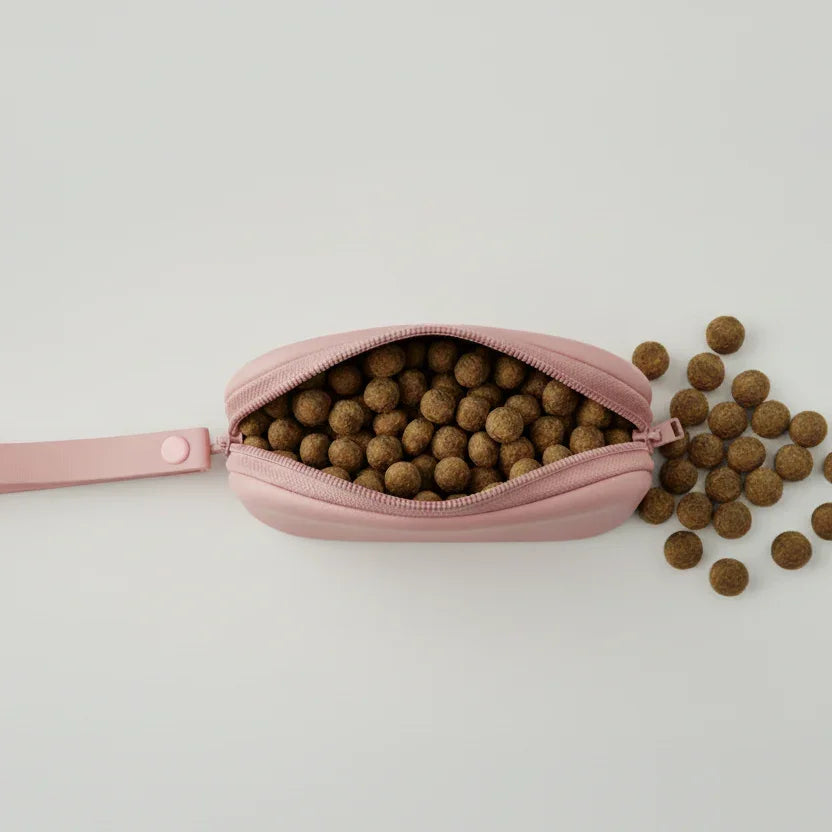 Pink zipper pouch filled with round pet treats spilling onto a white surface