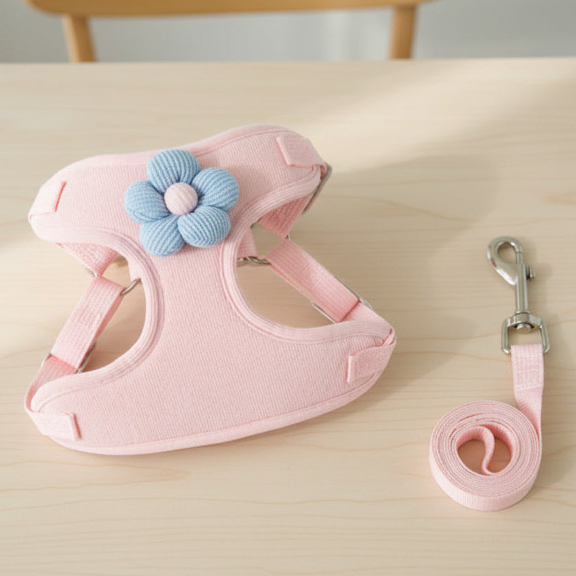 Pink pet harness with blue flower accessory and matching leash on light wood table