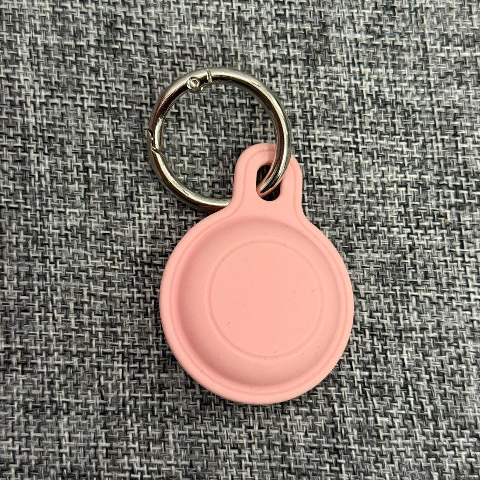 Pink silicone pet tag holder with metal keyring on a textured grey fabric background