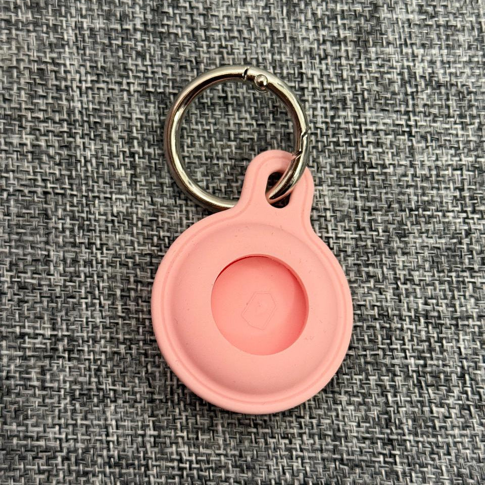 Pink silicone pet tag holder with keyring on textured grey fabric background