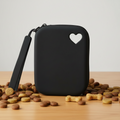 Black pet treat pouch with heart cutout surrounded by dog biscuits on wooden table