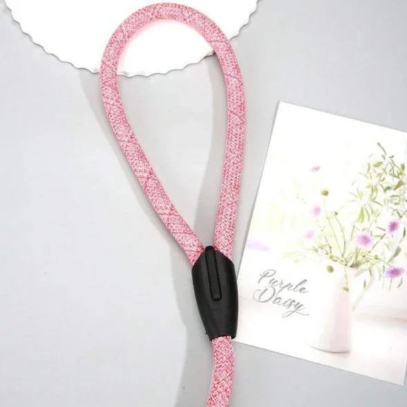 Pink rope pet collar with black clasp on a gray surface beside a floral card