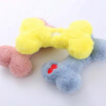 Plush bone-shaped dog toys in yellow, pink, and blue for pets on a white background.