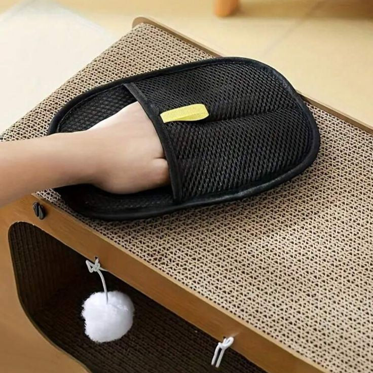 Hand in black mesh cleaning glove on cat scratching pad with toy ball attached